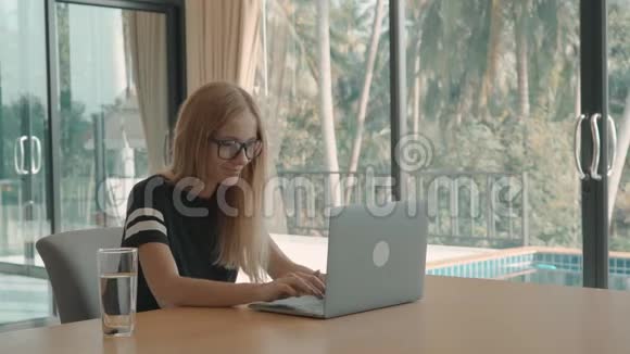 金发女人在她的桌子上打字窗外的游泳池自由职业概念视频的预览图