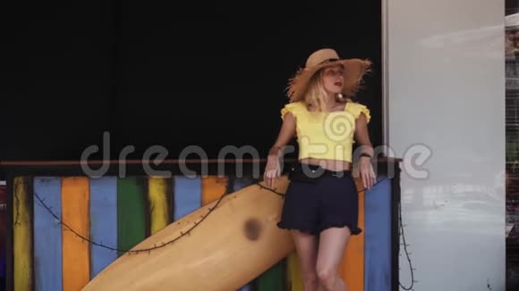 穿短裤和草帽的年轻美女站在冲浪板旁边视频的预览图