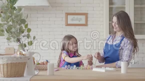 小女孩拿着复活节彩蛋用小刷子和妈妈一起画一个幸福的家庭筹备视频的预览图