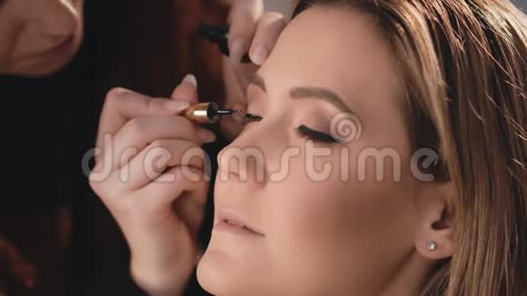 化妆师轻轻地在眼睛的眼皮上放一根黑色的湿眼线用专业的刷子刷在眼睛的脸上视频的预览图