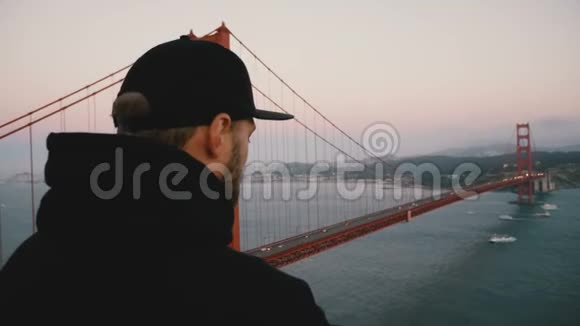 后景年轻的快乐游客穿着黑色的衣服拍电话照片雄伟的日落金门大桥加利福尼亚州视频的预览图