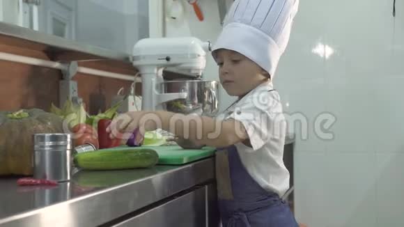 小男孩厨师穿着围裙做饭厨师帽在餐厅厨房做饭有趣的小厨师切鲜菜视频的预览图