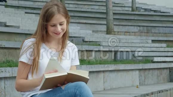 公园里年轻漂亮的女孩正在看书一个学生正在学习一本书翻页混凝土上的裂缝视频的预览图