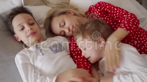年轻的母亲和她的两个儿子穿着睡衣周末一起在床上玩耍很懒视频的预览图