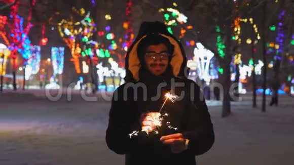 戴眼镜的印度男人晚上在公园里举着孟加拉灯和微笑视频的预览图