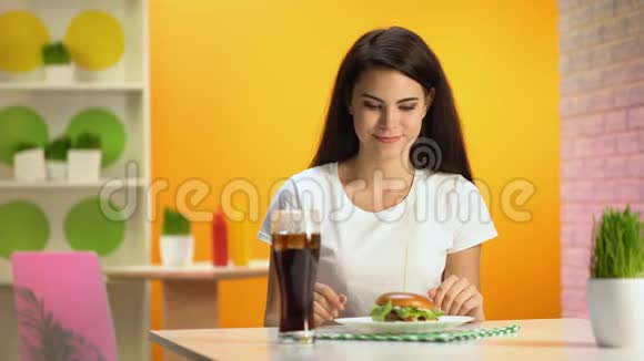微笑的黑发女人从盘子里拿着美味的汉堡快餐店视频的预览图