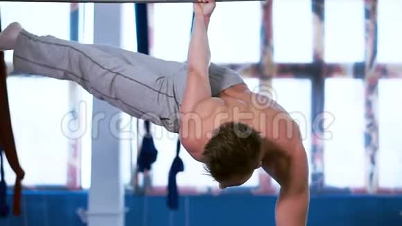 年轻的肌肉男在水平杆上锻炼挂在一只手臂上视频的预览图