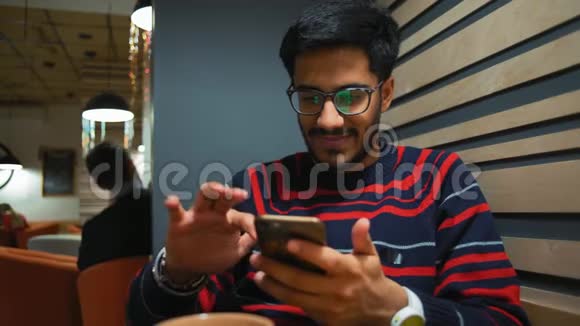 印度男人在智能手机上扫描新闻坐在咖啡馆里微笑视频的预览图