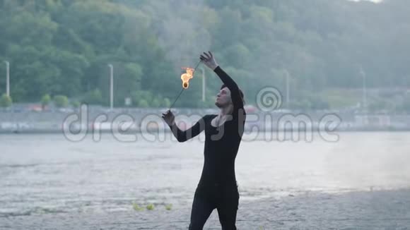 穿着黑色衣服的年轻人站在河岸上表演一场焰火表演有技巧的炉火艺术家呼气视频的预览图