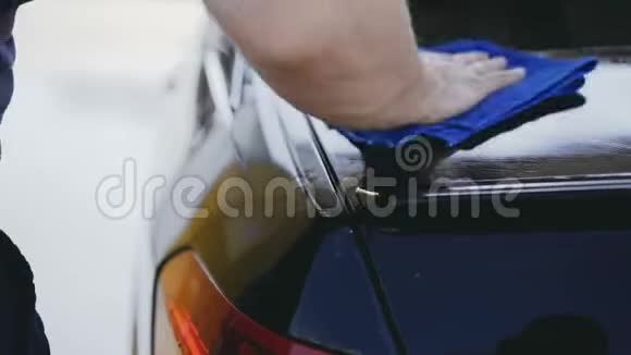 一个男人拿着一件蓝色的纺织品擦拭一辆黑色的汽车视频的预览图