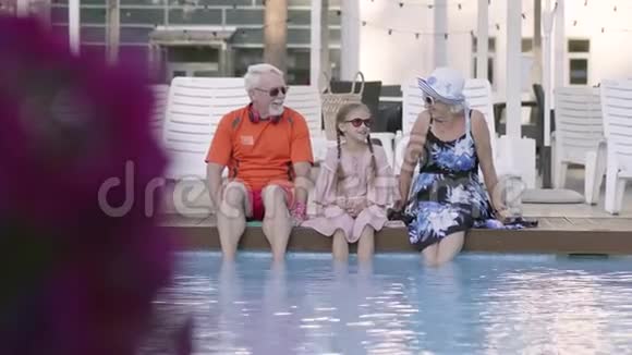 有趣快乐的成熟夫妇和小孙女坐在豪华游泳池的边缘祖母祖父和视频的预览图