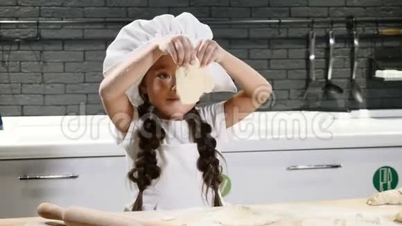漂亮的可爱女孩戴着厨师帽在厨房里玩面团和面粉儿童厨师概念小孩玩大人游戏视频的预览图