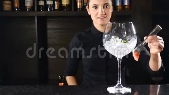 穿着黑色制服的女调酒师把一个草莓放进杯子里冰块准备鸡尾酒快乐酒保概念视频的预览图