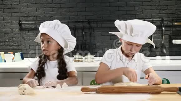 可爱的学龄前儿童在私人厨房里扮演真正的厨师穿白色围裙和厨师帽的儿童使用擀面杖视频的预览图