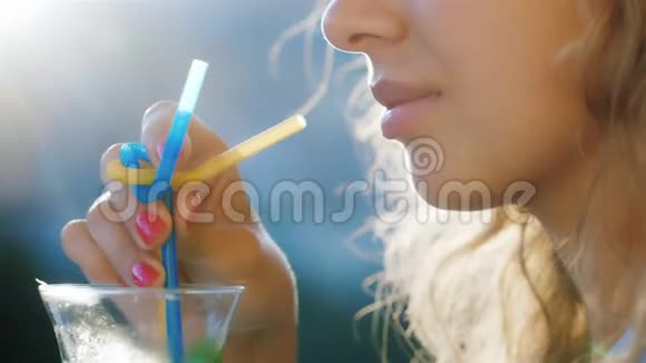 年轻女子在玻璃杯里搅动饮料在图片中可以看到阳光照耀的嘴唇和头发概念a视频的预览图