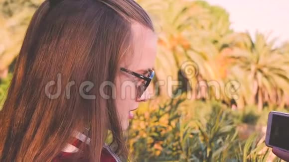 少女在棕榈树附近的智能手机上拍摄维多西班牙巴塞隆游客视频的预览图