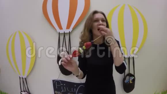 优雅的女人穿着黑色连衣裙在棍子上吃各种水果关节活动度射击视频的预览图