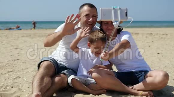 在阳光明媚的夏日幸福的一家人在海边休息一个男人一个女人和一个孩子坐在海滩上拿着一个视频的预览图