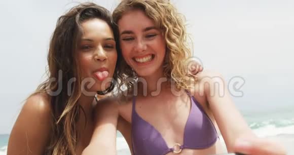 两位混血女朋友在海滩上用手机自拍的正面景色视频的预览图