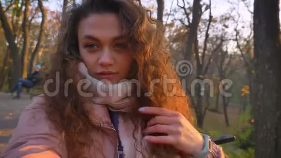 白种人卷发女人在秋公园修头发和制作自拍照片的自我视频视频的预览图