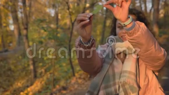 秋日公园绿叶上观看的年轻白种人卷发女子肖像视频的预览图