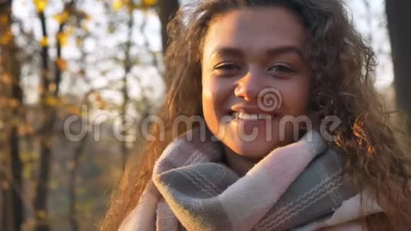 白种人卷发女人的肖像微笑着看着镜头在秋天公园的背景上转向太阳视频的预览图