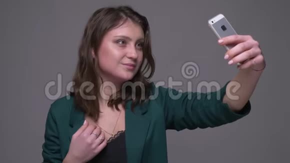 成年迷人的深色头发的女性在手机上自拍的特写镜头背景是灰色的视频的预览图