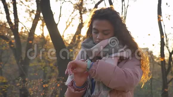 围绕着白种人卷曲头发的女人的肖像在秋天公园的背景下看手表视频的预览图