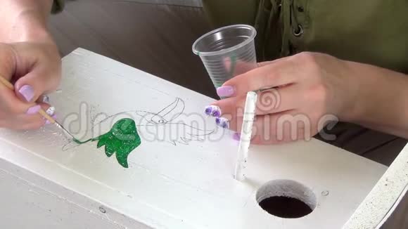 在夏日一个长满绿葡萄的凉亭里女人在一个木制筑巢箱上画图案视频的预览图