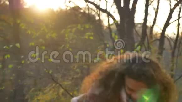年轻的白种人卷发女子在阳光明媚的秋天公园里收集树叶并检查它们的肖像视频的预览图