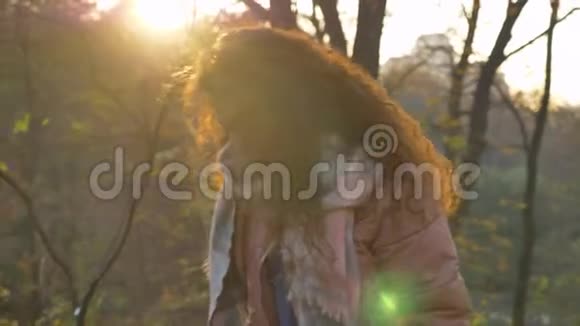 年轻的白种人卷发女子在阳光明媚的秋日公园散步和翩翩起舞的树叶的肖像视频的预览图