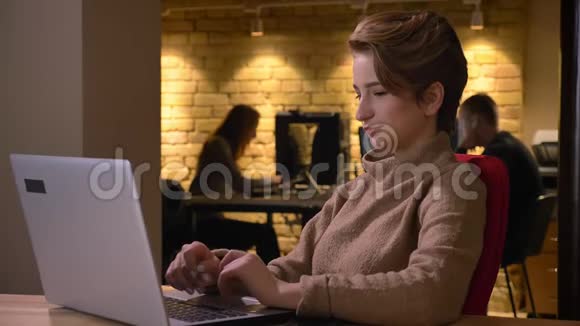 快乐的年轻女性的肖像短发笑着在办公室的笔记本电脑上打字视频的预览图