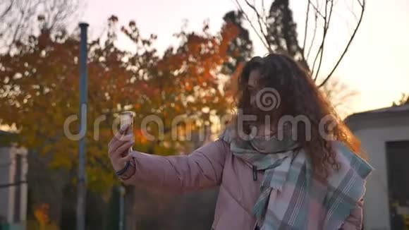 在秋日的时候白种人卷发女孩用智能手机摇着头发制作自拍照片视频的预览图