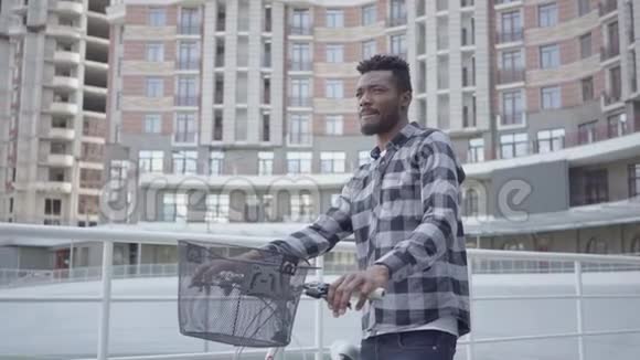 英俊的非裔美国人站在城市建筑的背景下骑着自行车他正在休息视频的预览图