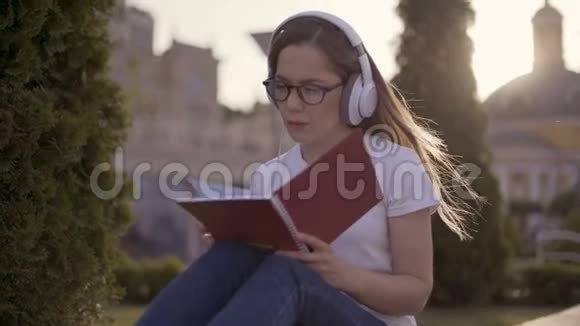 专注的女学生在公园里坐在草地上学习女孩手里拿着笔记本听着视频的预览图