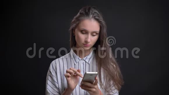 美丽的白种人长发女人在黑色背景下体贴地与智能手机合作的肖像视频的预览图