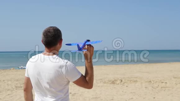 一个人站在海滨在一个炎热的晴天发射一个不规则的飞机进入天空小飞机飞视频的预览图