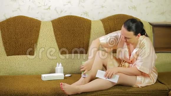 沙发上的一位年轻女士用餐巾从腿皮上取下蜡视频的预览图