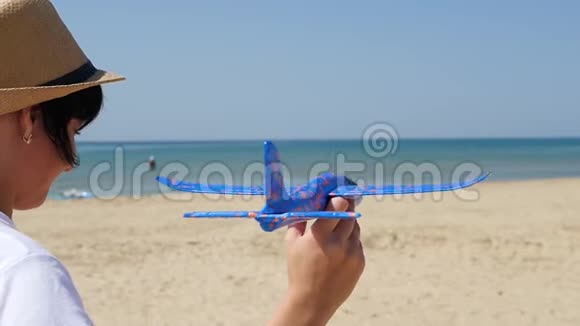 一个女人站在海滨在一个炎热的晴天并发射一个不规则的飞机进入天空小飞机飞视频的预览图