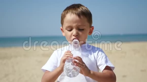 一个可爱的小宝宝在炎热的晴天站在海滩上喝瓶子里的水休闲和游戏视频的预览图
