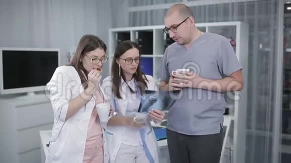 一组医生检查X光在工作人员房间喝一杯热饮料医生看了看X光片视频的预览图
