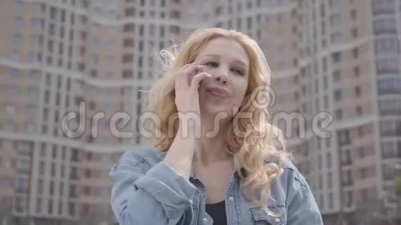在摩天大楼前用手机说话的漂亮微笑自信的金发女人的特写脸城市生活方式视频的预览图