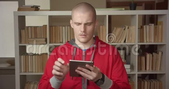 一幅年轻迷人的白种人男学生的特写肖像他在平板电脑上发短信看着大学里的摄像机视频的预览图