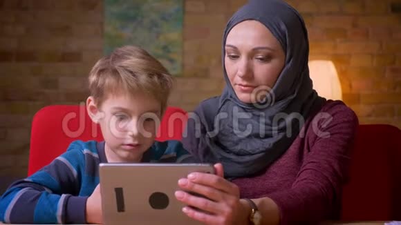 小男孩和他的穆斯林母亲戴着头巾一起观看平板电脑并讨论的肖像视频的预览图