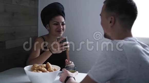 漂亮的年轻女人头上戴着浴巾正和男朋友或丈夫坐在厨房的桌子上有机会视频的预览图