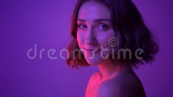 特写侧景拍摄年轻迷人的女性在镜头前摆着霓虹灯紫色背景视频的预览图