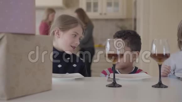 描绘了三个有趣的孩子坐在桌子旁拿着小蛋糕和带果汁的酒杯两个白种人女孩和视频的预览图