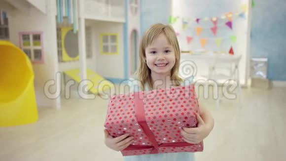 一个漂亮的小女孩在房间里的镜头前摆着一个大礼物盒视频的预览图
