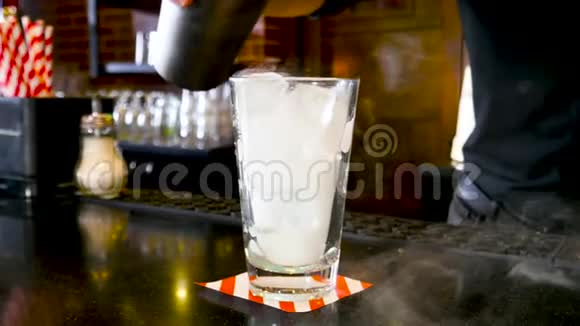 经典的酒保在室内一流的酒吧里把五颜六色的液体从摇床倒入带有白色冷烟的鸡尾酒杯视频的预览图