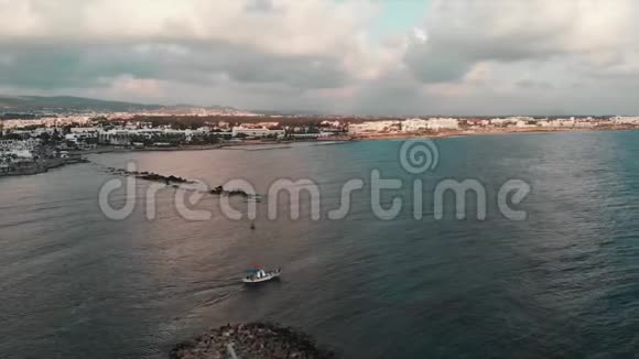 在日落时分从美丽的城市港湾向公海航行的白色小渔船的空中无人机景视频的预览图